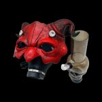 Red, ornate mask with a glass pipe beside it, isolated on a black background.