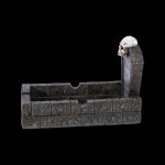 A gothic-style ashtray shaped like a stone castle wall with a skull-topped tower, designed for cannabis use.