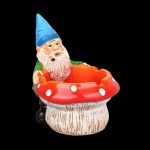 A whimsical garden gnome figurine seated inside a red mushroom-shaped ashtray, likely for cannabis use."