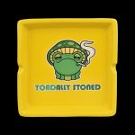 Yellow ashtray featuring a cartoon frog wearing a mushroom cap and exhaling smoke, with the text "TOADALLY STONED."