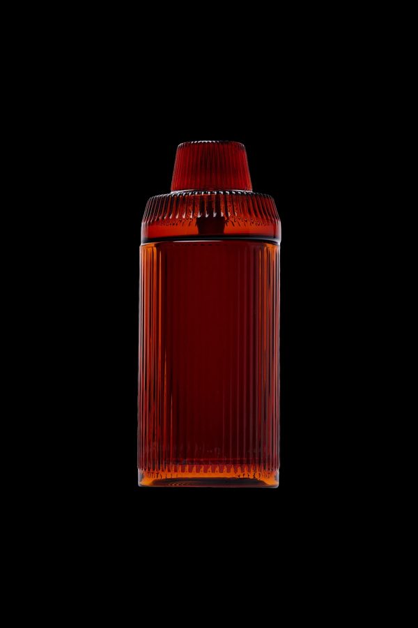 Amber glass cannabis storage jar with ribbed texture, isolated on a black background.