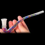 A hand holding a colorful glass pipe for smoking cannabis, against a black background.