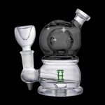 Clear glass rig with a dark grey dome and intricate detailing, featuring a green logo.