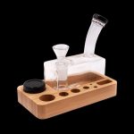 Glass bubbler and wooden organizer for cannabis accessories on a black background.