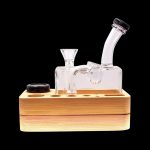 Clear glass dab rig with a wooden base and black carb cap, isolated on a black background.