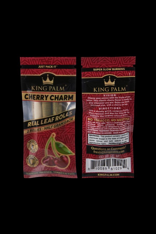 Close-up of two King Palm pre-rolled cones—"Cherry Charm" and "Vision"—in red packaging, highlighting the brand logo and flavor names, with text indicating “Terpene Infused - Tobacco Free” and a half-gram size.