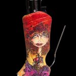A decorated lighter with a colorful, psychedelic portrait of a woman and a thin metal tool extending from its side, set against a black background.