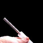 A hand holds a clear glass oil burner pipe against a black background.