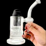 Clear glass rig with a bubbler and mouthpiece held in a hand, against a black background.