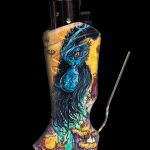 A lighter decorated with a vibrant, colorful dragon design and accompanied by a metal cleaning tool, set against a black background.
