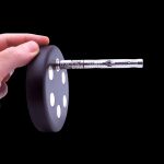 Silver dab straw inserted into a black silicone dab dish held by a hand, against a black background.