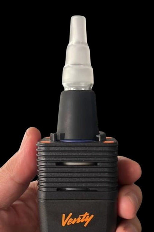 A hand holds a black and orange cannabis vaporizer with a glass mouthpiece.