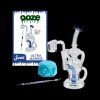 A studio shot of a clear glass water pipe ("rig") alongside cannabis accessories including a dab tool, silicone container, and product packaging for "Ooze Swell Ultra Marine."