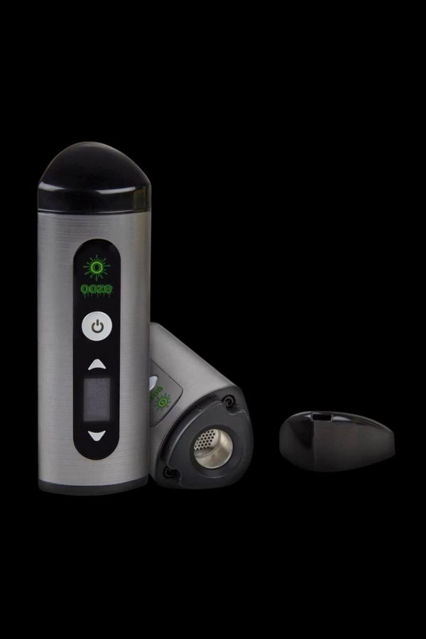 Silver and black cannabis vaporizer with illuminated green controls, displayed with open chamber.