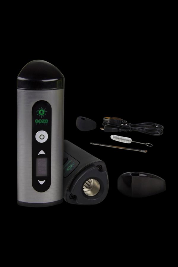 Silver cannabis vaporizer pen with included mouthpiece, cleaning tools, and charging base displayed on a black background.