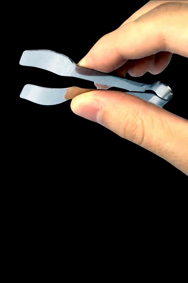Silver cannabis trimming scissors held in a hand, against a black background.