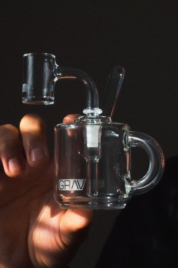 Hand holding a clear glass rig with a dab nail, branded with "GRAV."