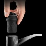 Hand holding a black vaporizer component above a glass pipe, product shot.