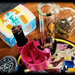 Close-up of cannabis smoking accessories including a glass pipe, grinder, lighter, and ashtray."