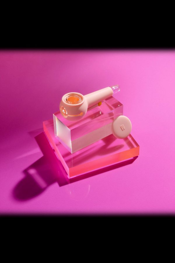 Pink glass cannabis pipe and concentrate on acrylic display, illuminated with pink light.