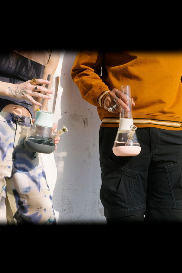 Two people holding glass bongs, partially visible against a textured wall.