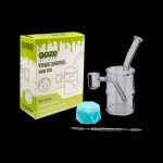 Ooze Toxic Barrel dab rig kit with glass water pipe, quartz banger, dab tool, and blue ice cube cooling insert, displayed with its packaging.